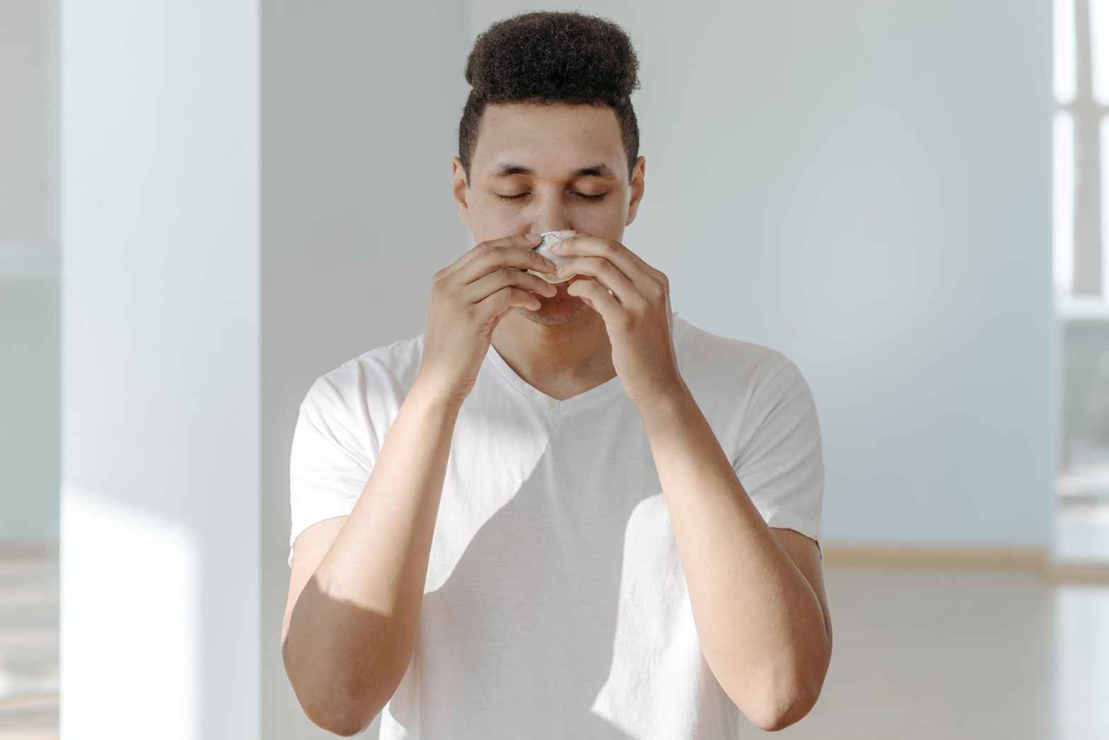 sick man in white shirt wiping his nose with tissue